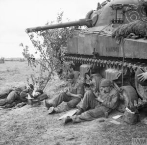 10 juin 1944 : l'équipage d'un char M4 Sherman appartenant à l'escadron C, 13th/18th Royal Hussars, 27th (GB) Armoured Brigade, profite d'un moment de détente sur le front normand pour se reposer ou rédiger une lettre. Photo : IWM B 5425