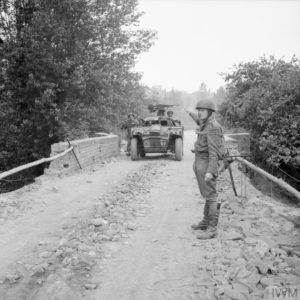 Le 16 juillet 1944 dans le cadre de l'opération Pomegranate, un soldat britannique de la police militaire guide un véhicule de reconnaissance Humber Scout Car qui traverse la rivière Odon. Photo : IWM B7594